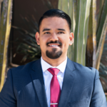 Jesus Chavez wears a grey suit with a red tie and white shirt.