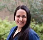 Rachel Fernandez is standing in front of blurred area of foliage wearing a blue blazer.